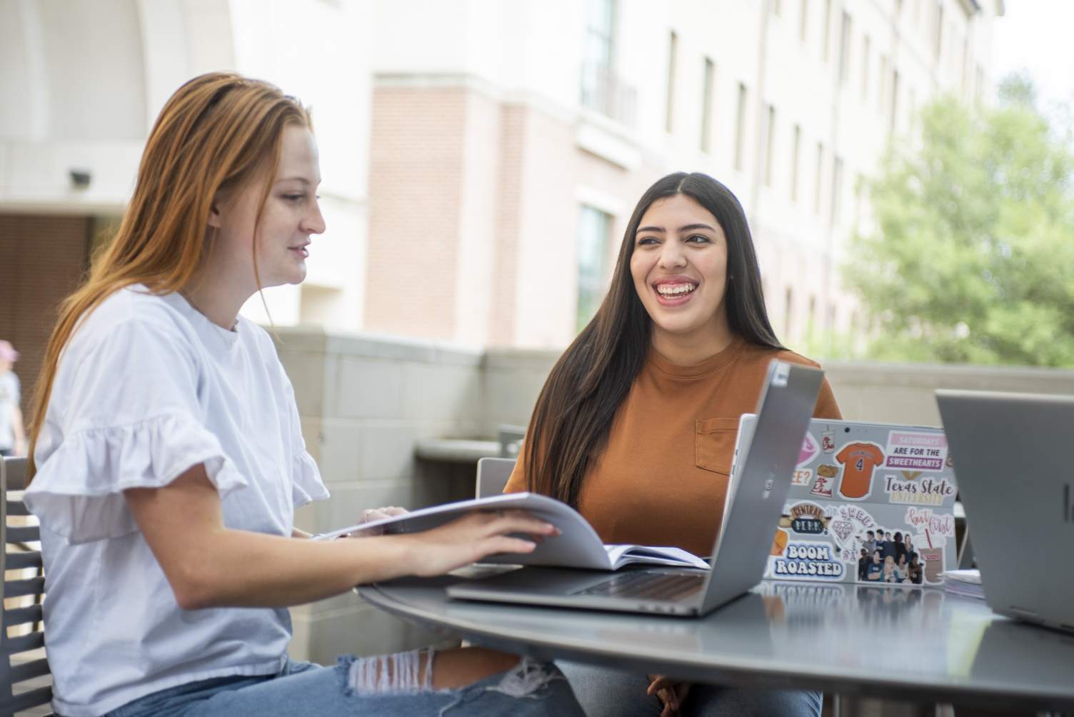 Pair of students sit at a table on TXST campus on laptops