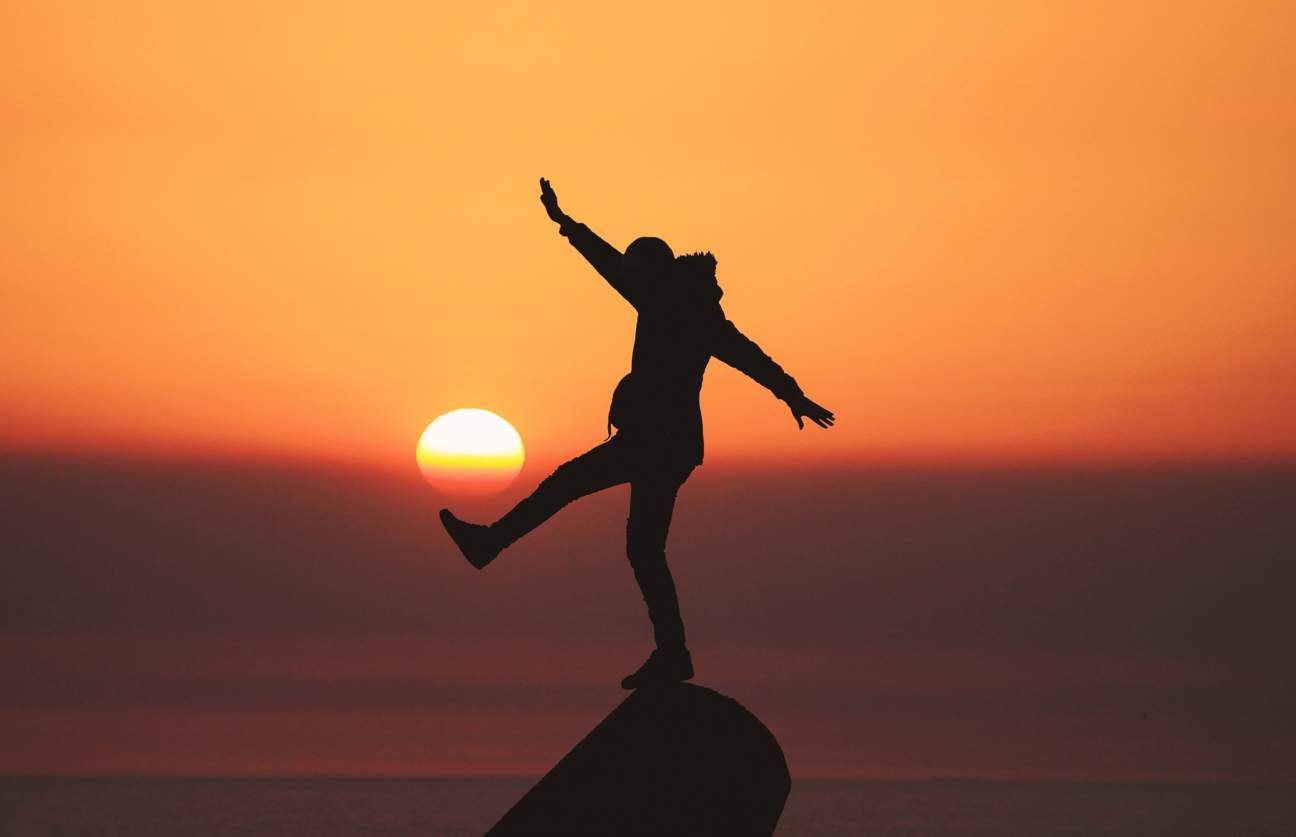 a person standing on a rock with the sun in the background