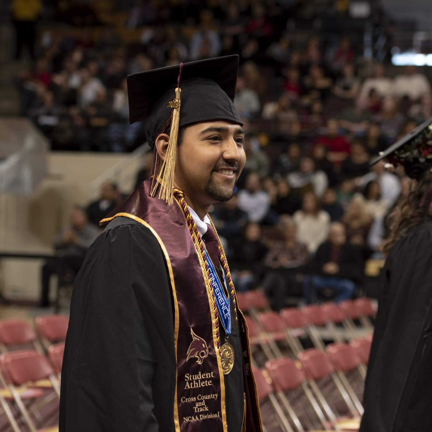 graduate walking down aisle wearing student athlete stole and medal