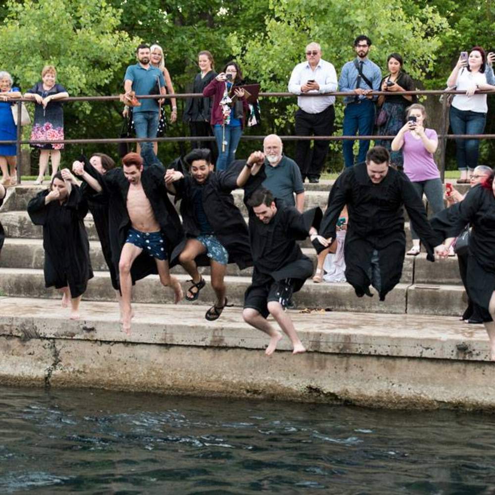 group holding hands as they jump into the river