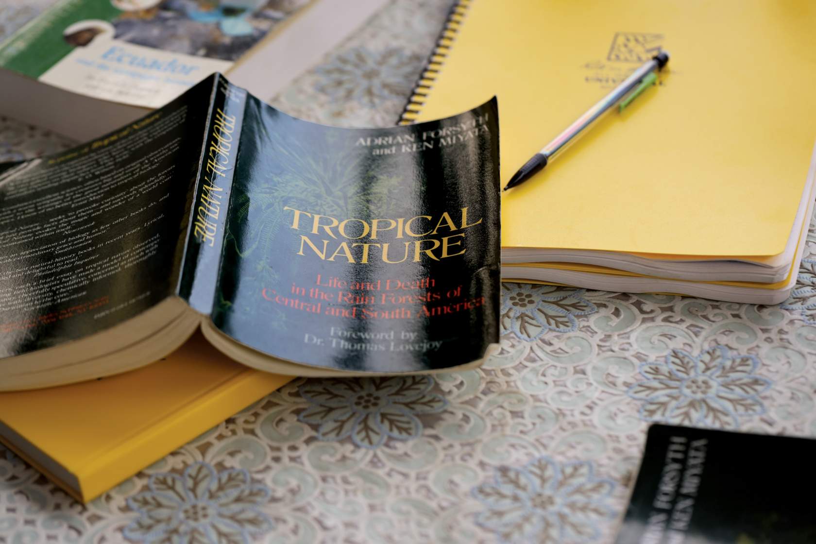 a copy of the book "Tropical Nature" lies open on a table on top of two notebooks