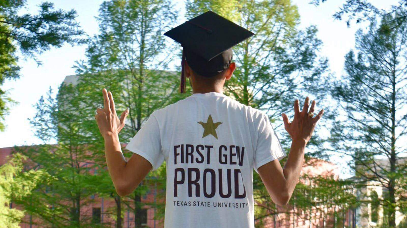 Student facing away wearing First-Gen Proud shirt and making Texas State handsigns.