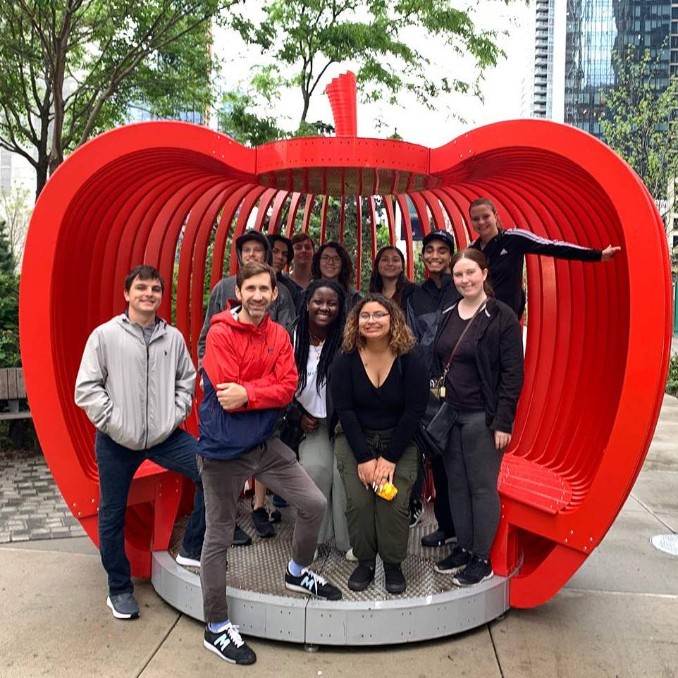 students and staff standing in large red apple sculpture