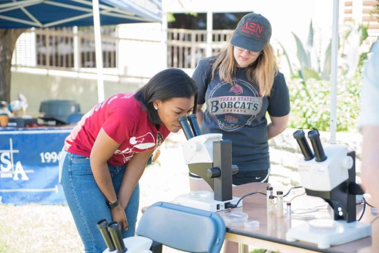 student watches a girl look through a microscope