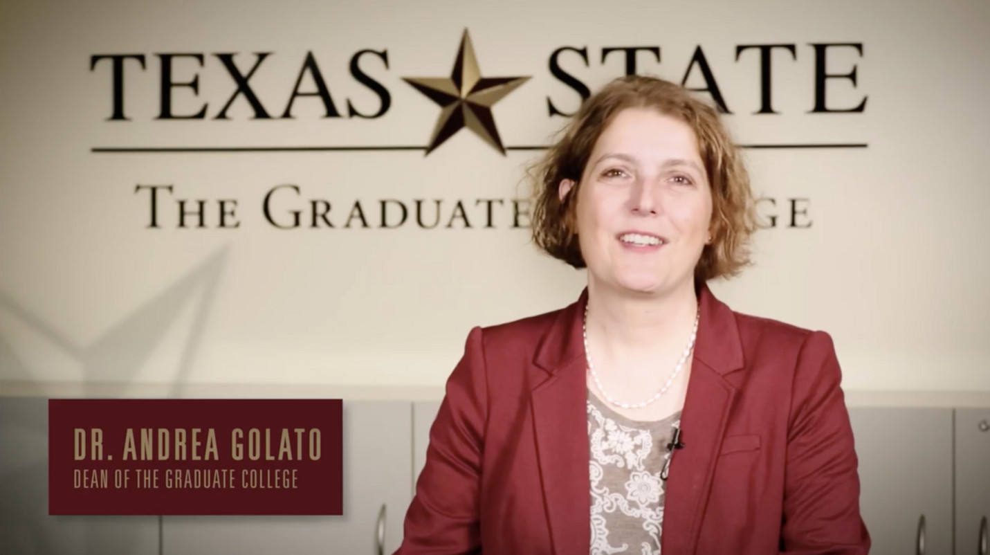 Dr. Andrea Golato, Dean of the Graduate College, smiles in front of a Texas State logo