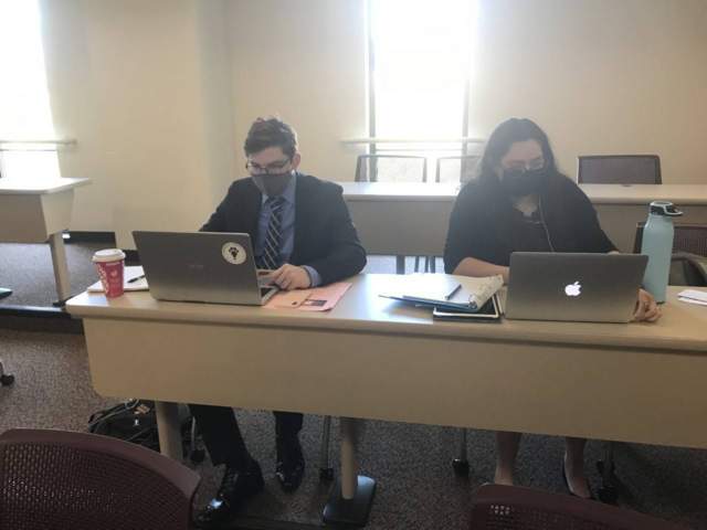 male and female students dressed professionally sitting at desk behind laptop