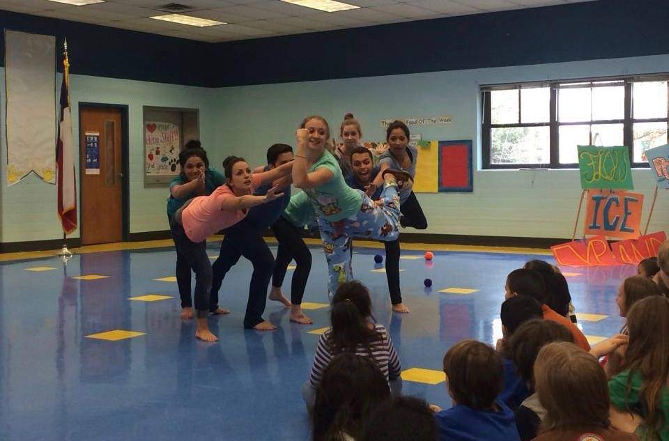 a group of dancers dancing in a classroom stage in front of elementary students