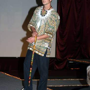 Student wearing a multi-colored print caftan style shirt, dress slacks, white loafers and carrying a cane.