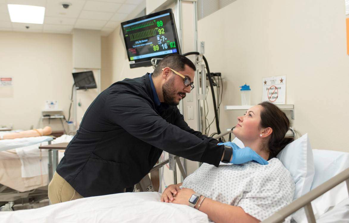 Hispanic man practices the nutrition focused physical exam on a patient in a hospital bed