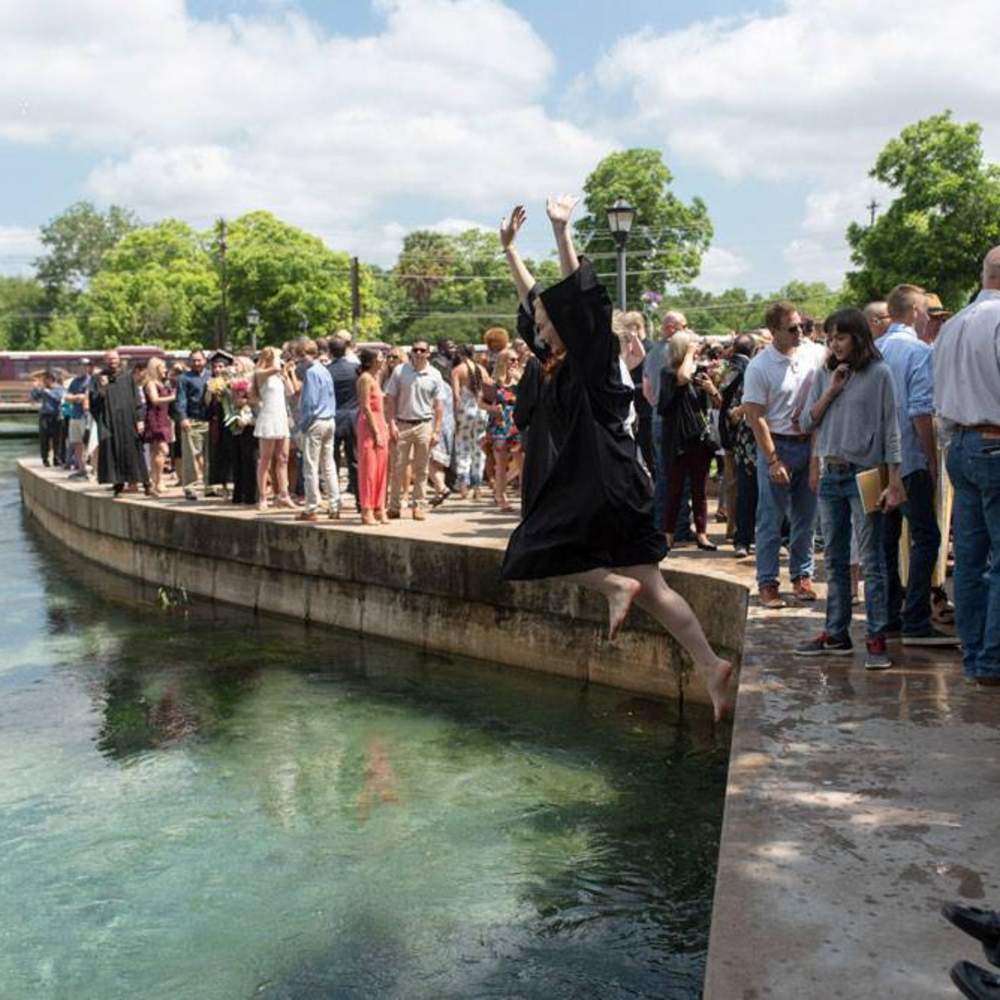 graduate jumping with hands up into the river