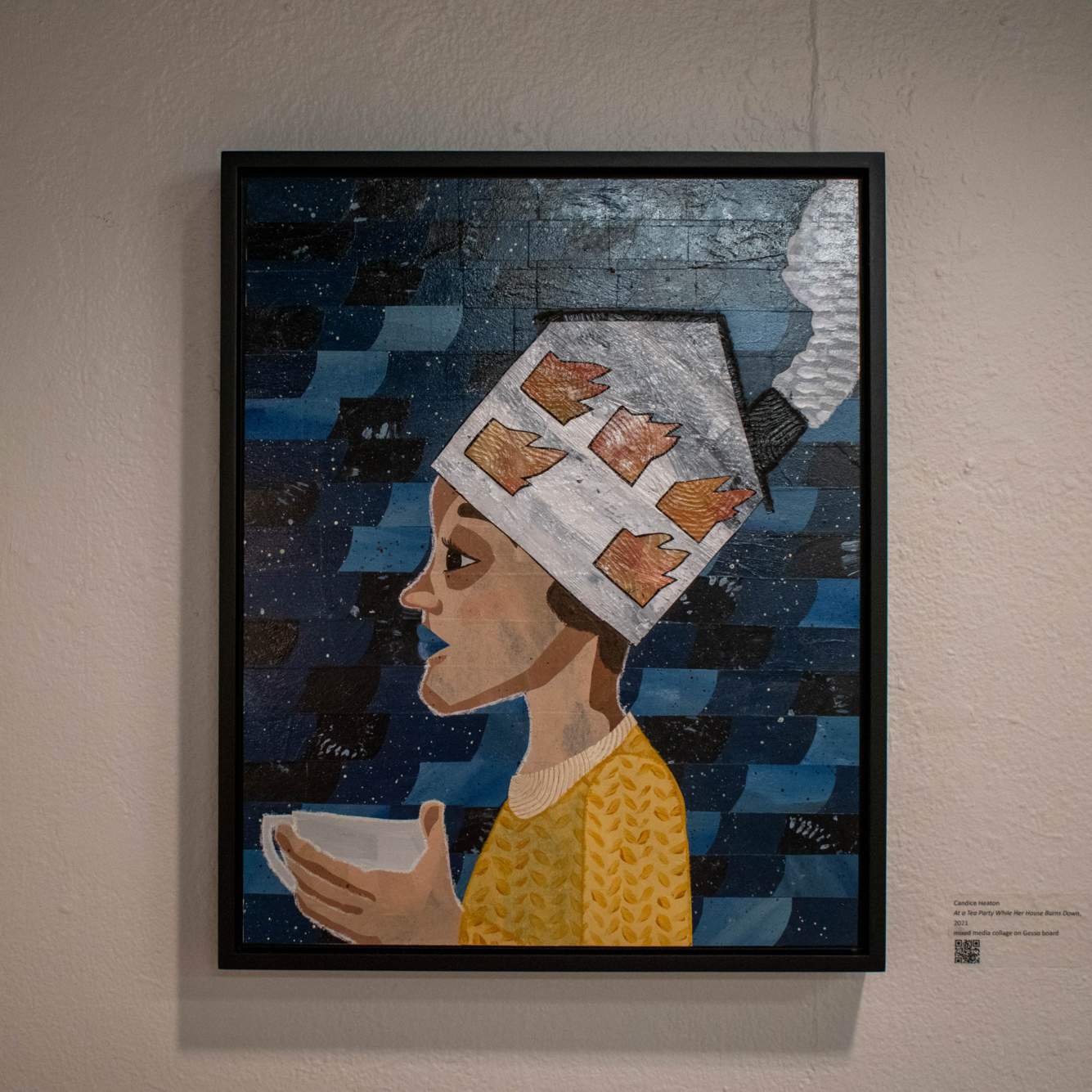 Gesso and mixed media textured painting of a woman with a burning house as a hat while holding a tea cup on a multi-blue background. Hung on a white wall.