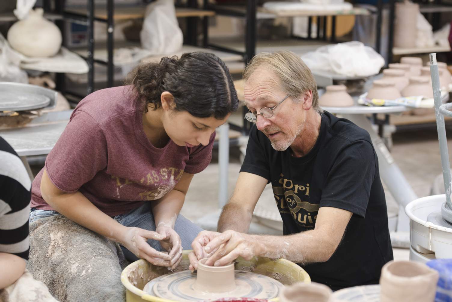 A female student works on pottery with professor