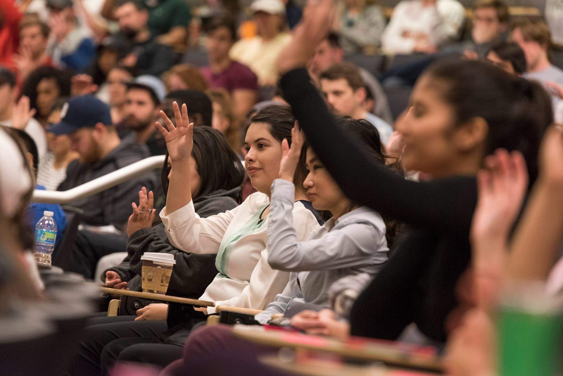 students raise their hands in a large lecture hall