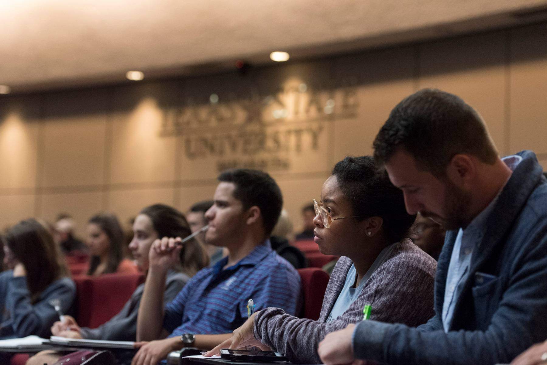 Students in a lecture hall, listening to a lecture.