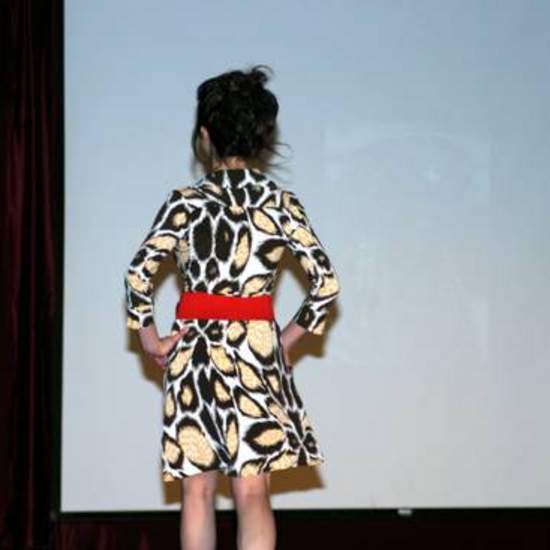 back view of student wearing an animal print dress, red beat and a red purse. 