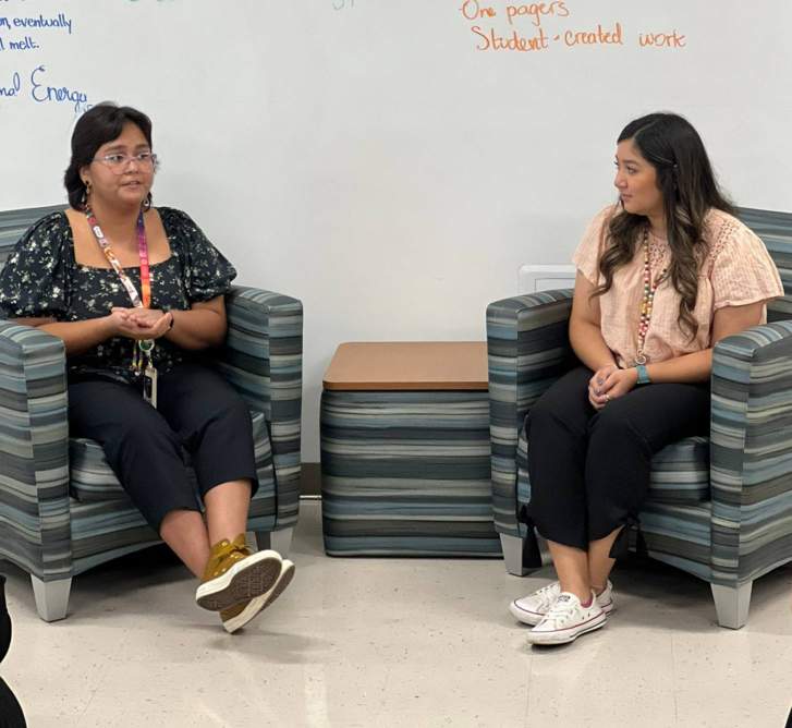 two females sitting in chairs in front of white board