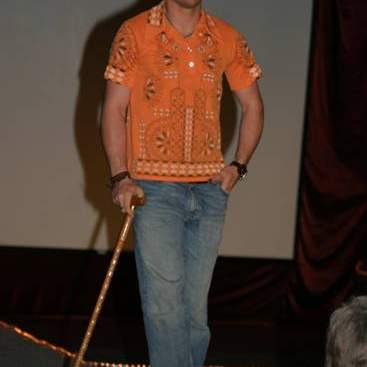 Student wearing orange print short-sleeved shirt, jeans, sneaker and carrying a cane.