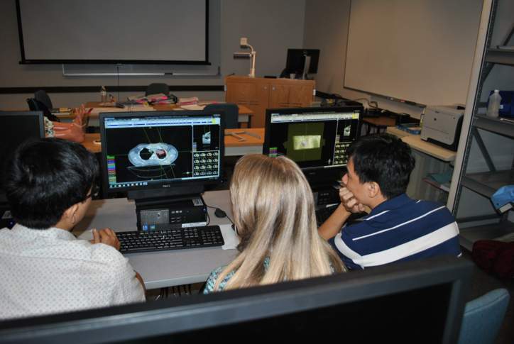 Three students watching a monitor with medical imaging in the Radiation Therapy treatment planning computer lab