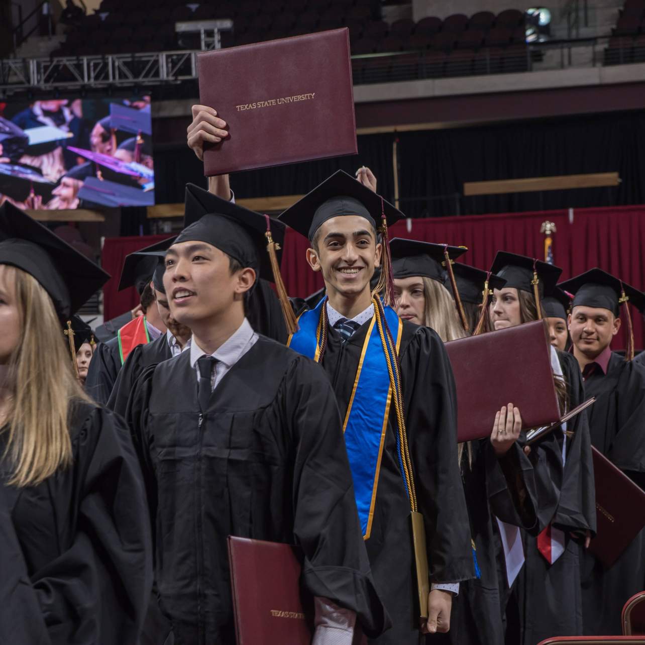 graduates walking down aisle, holding diploma overhead