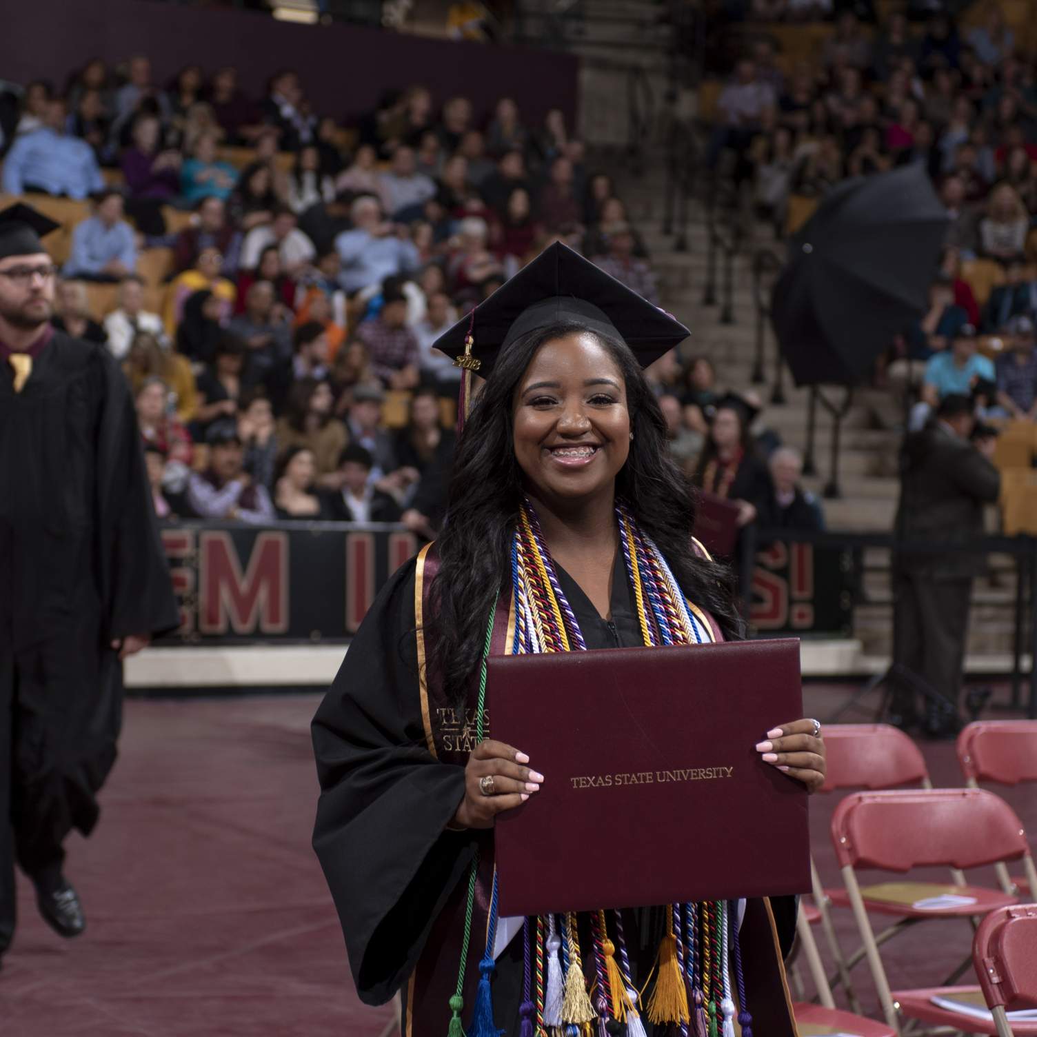 graduate smiling, holding diploma walking down aisle