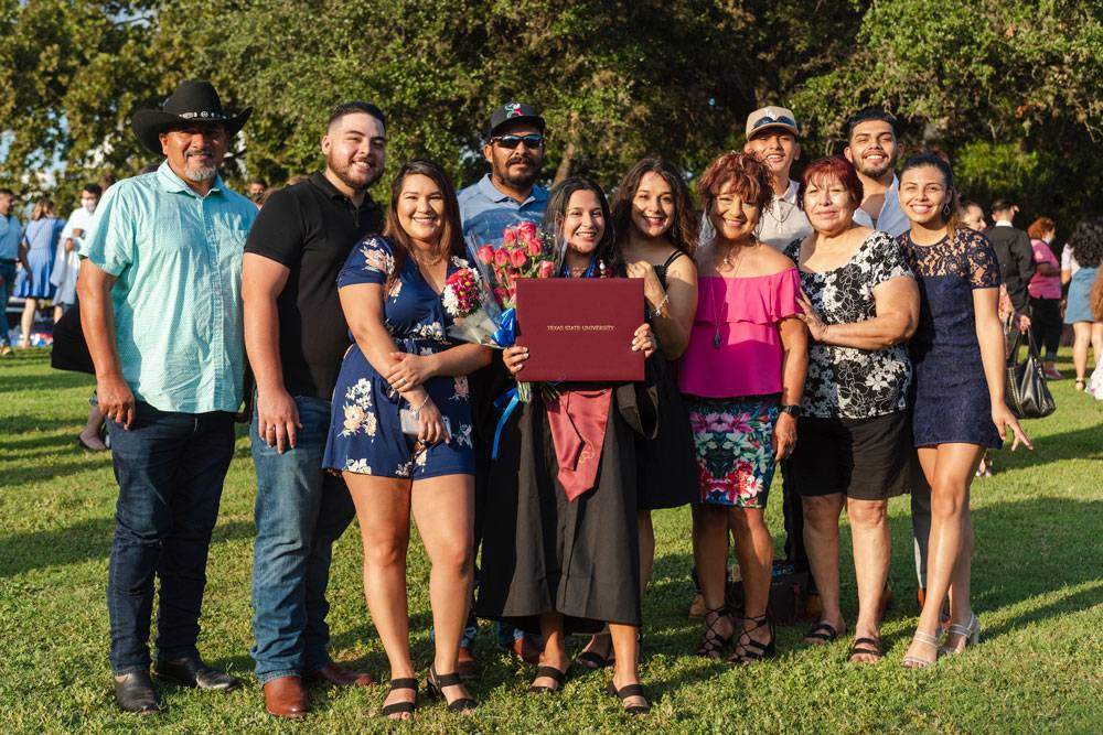 Una estudiante graduada de TXST tiene su diploma, rodeada de familia