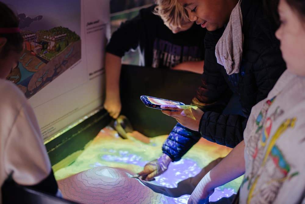Students learning about watersheds at sandbox exhibit in Disovery Hall