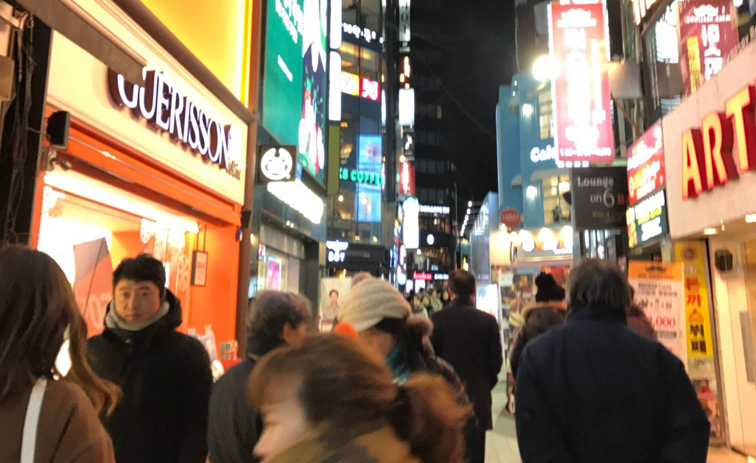 a busy street with brightly lit, neon storefronts in Seoul, South Korea