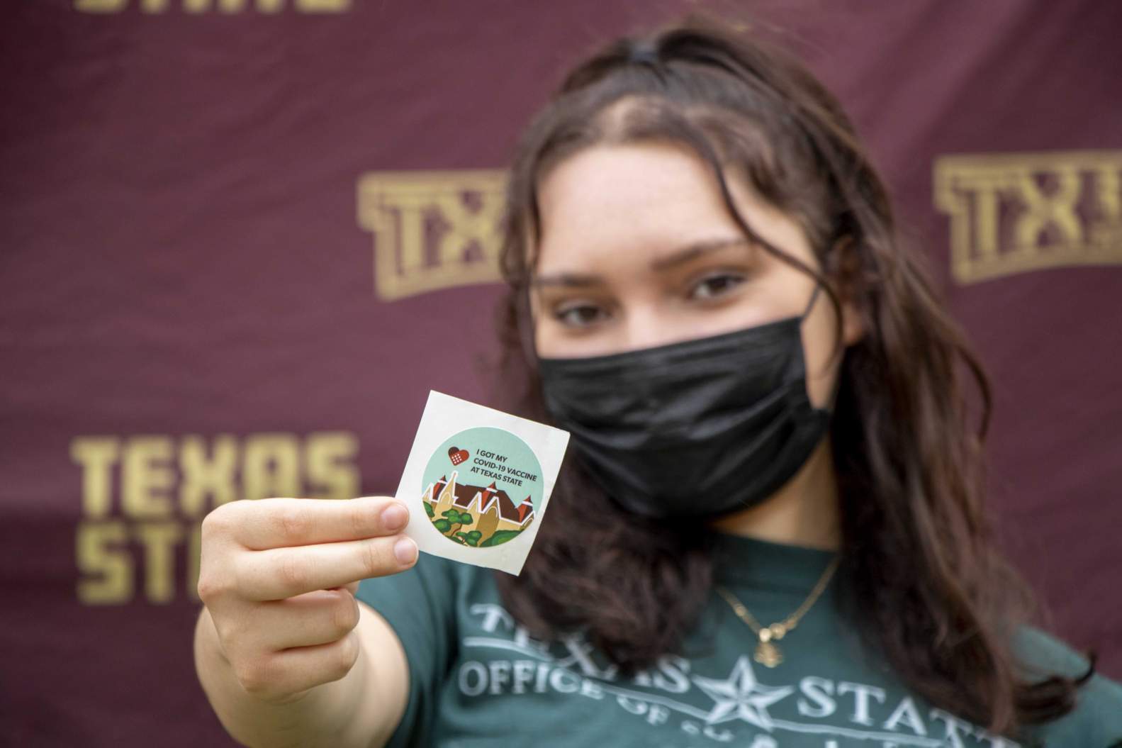 Student with mask holding a sticker for receiving a COVID-19 vaccine