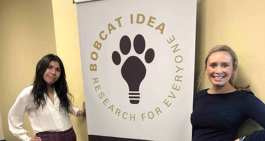 two women standing next to bobcat idea sign