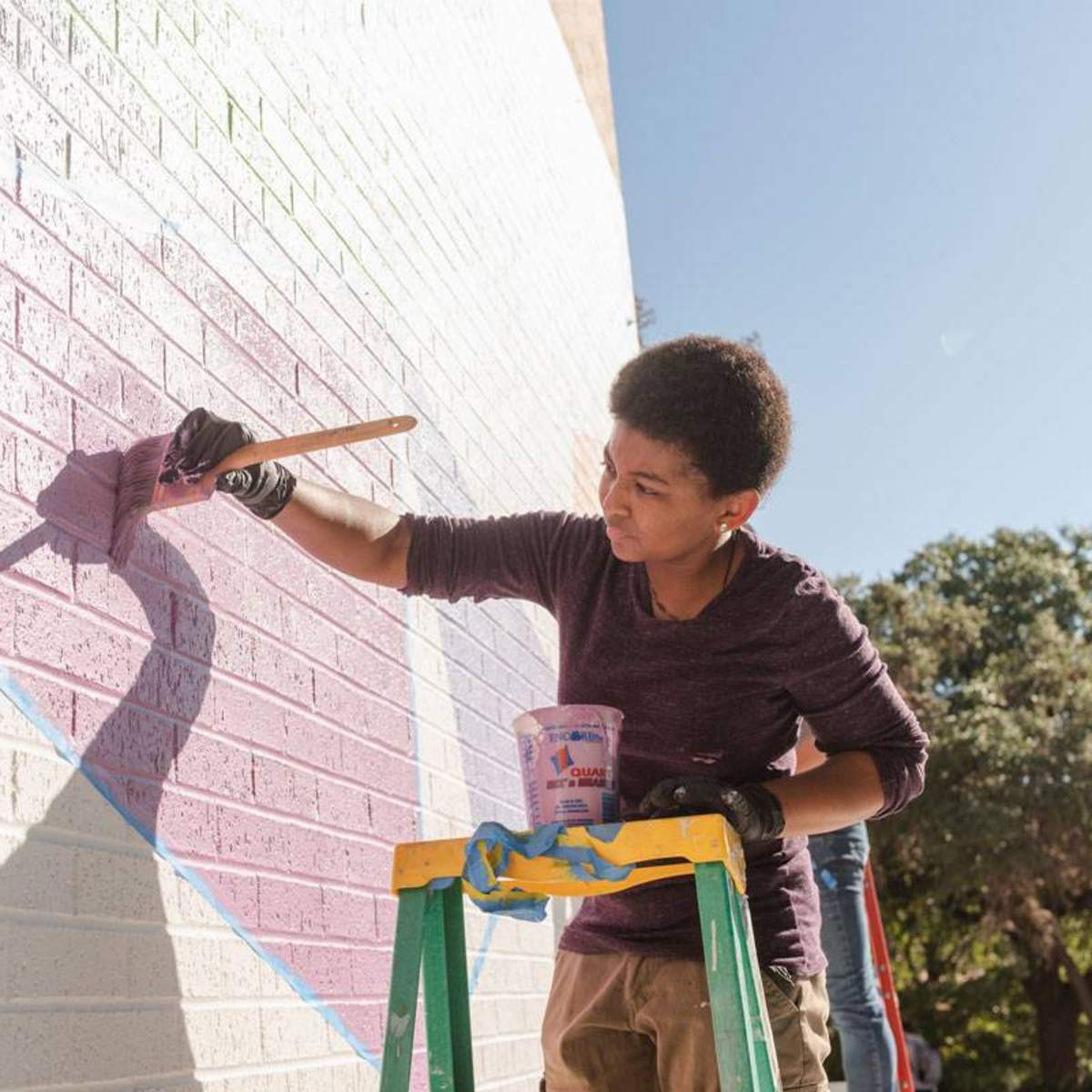 student on ladder painting with purple