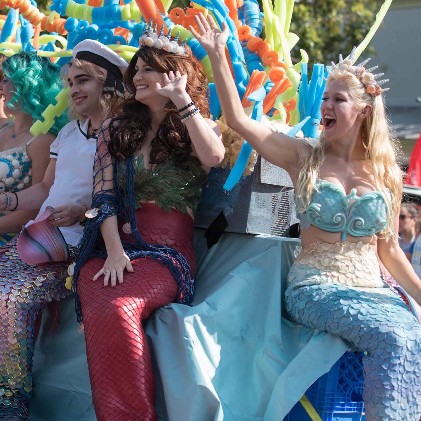 a car full of people dressed as mermaids passes by during the mermaid parade