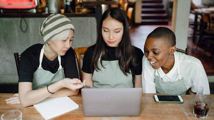 Three people sitting at table looking at laptop
