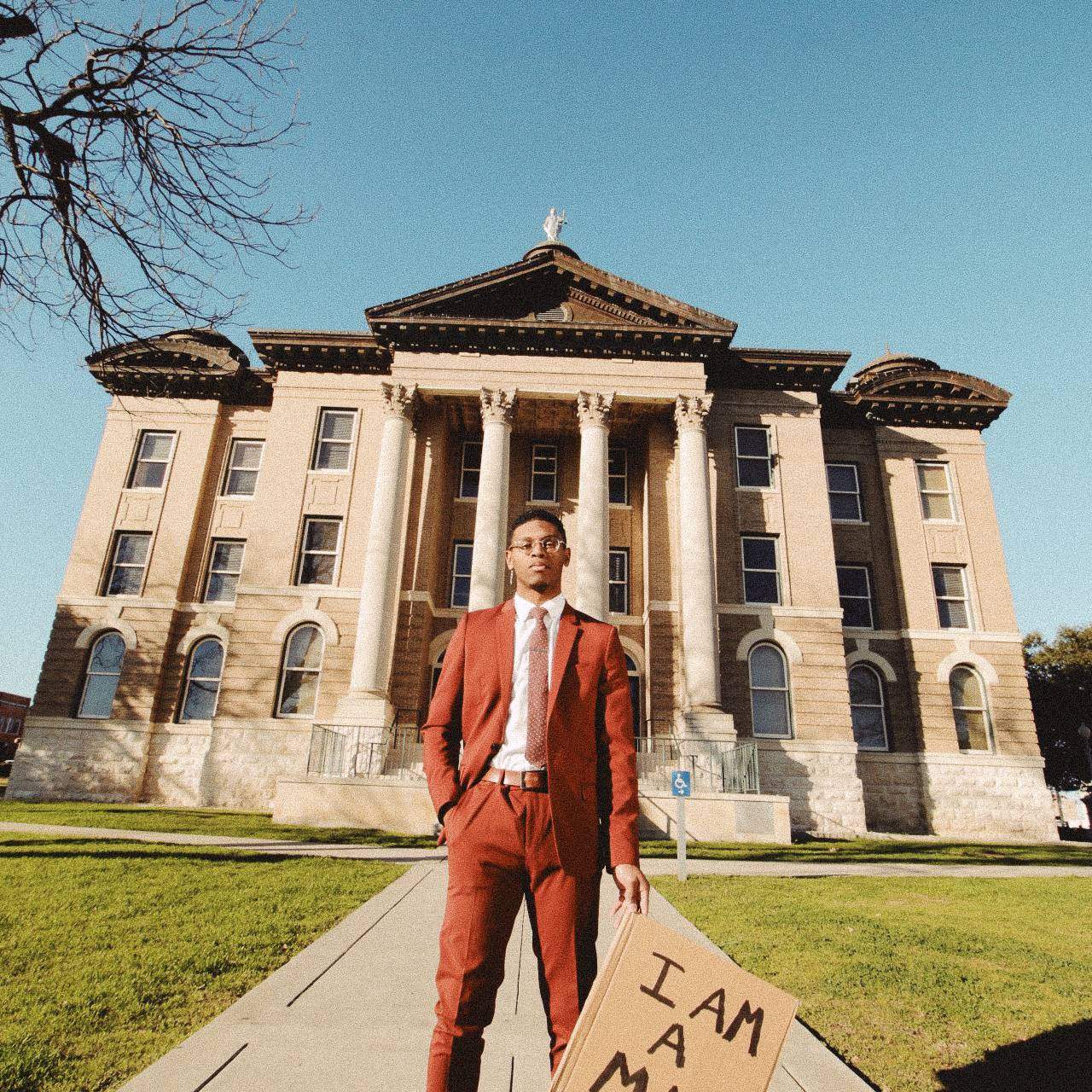man in red suit standing in front of court house with sign
