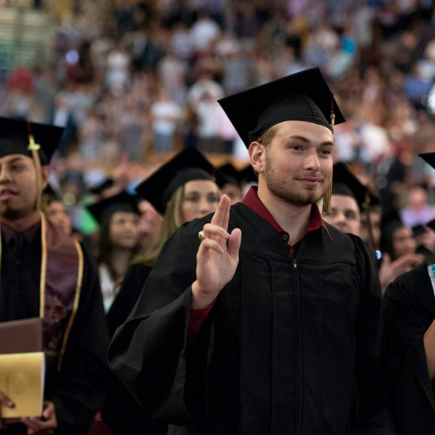 graduates holding up txst hand sign