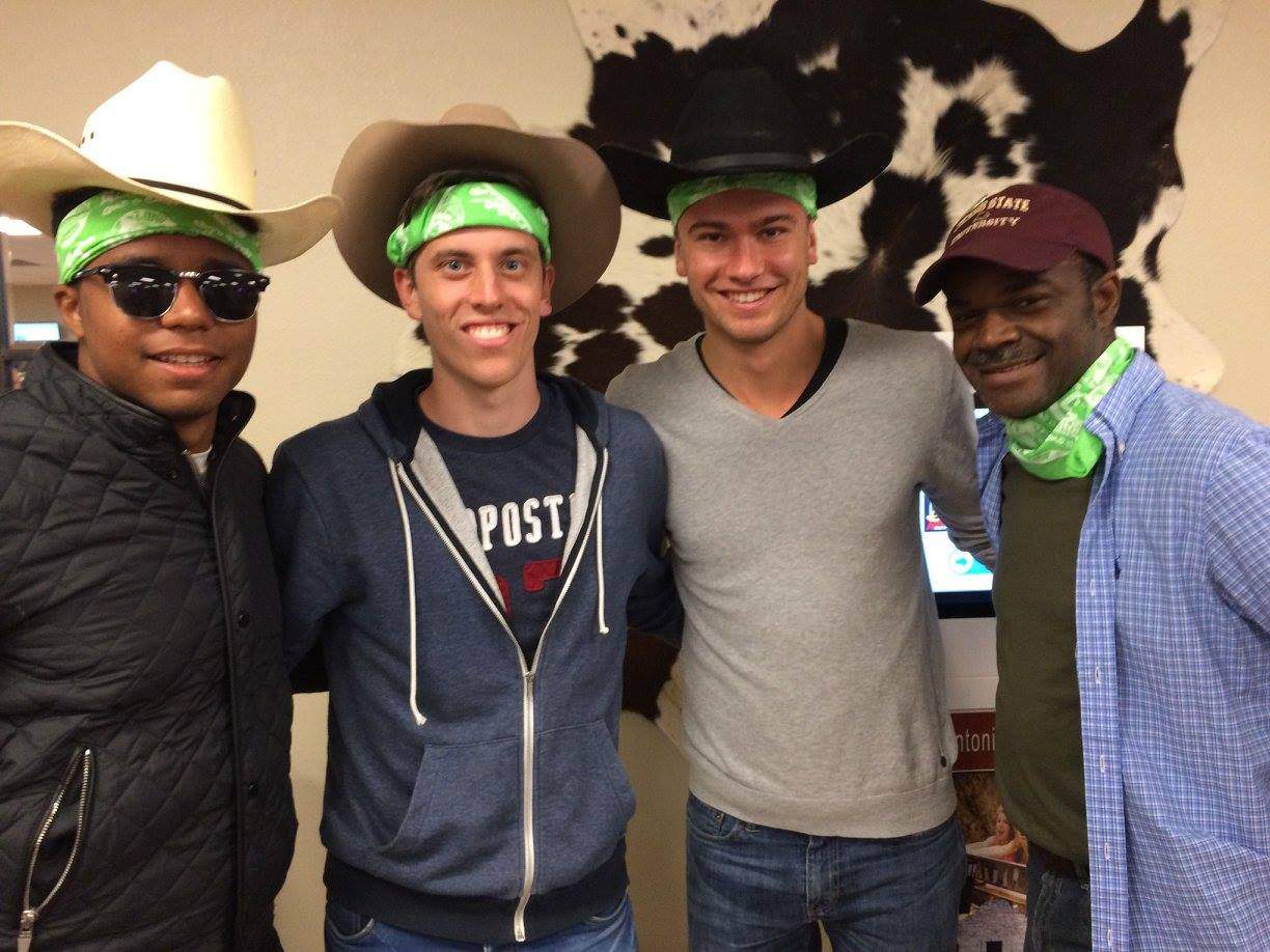 Group of students wearing cowboy hats and green bandanas smile for a photo