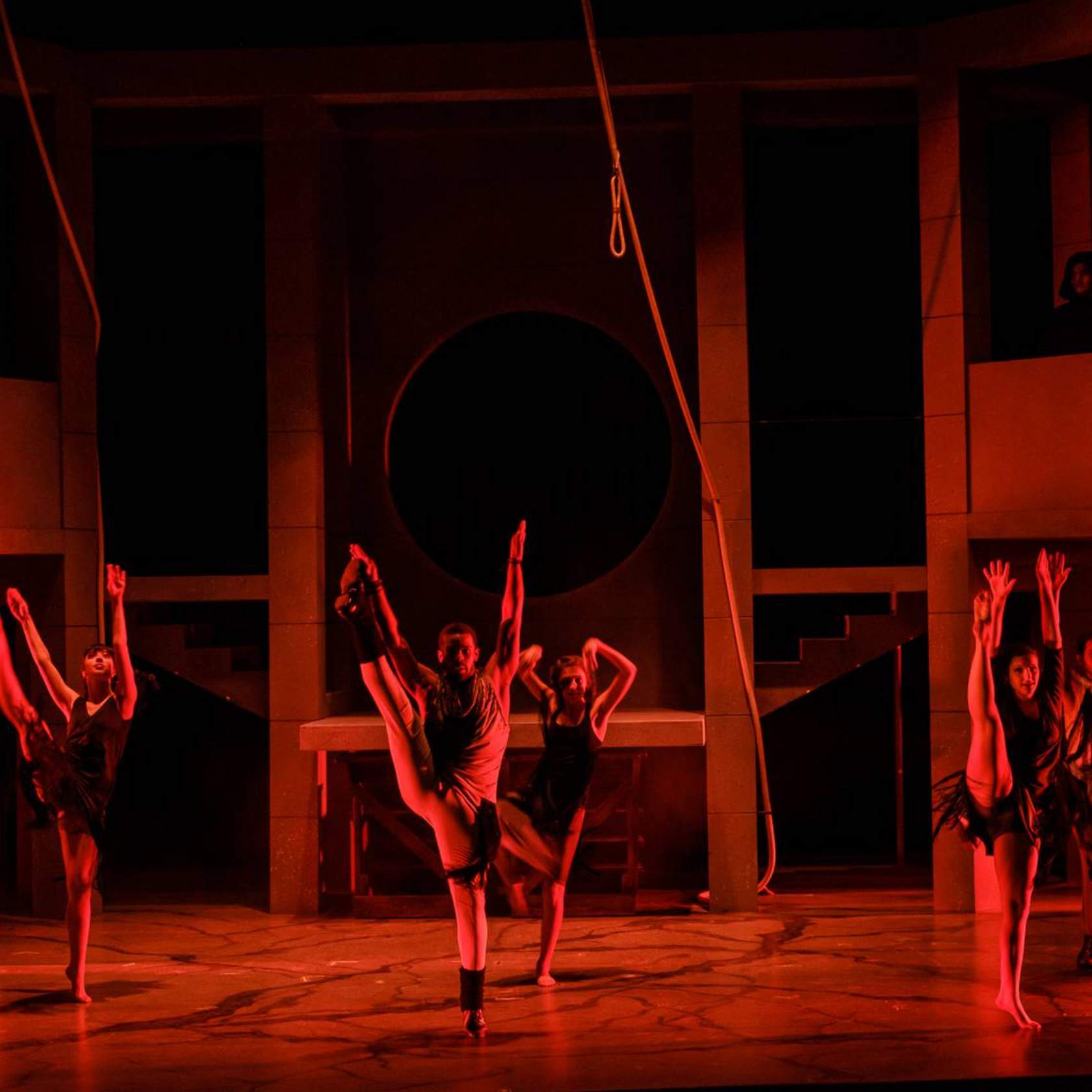 Dancers with legs raised, lit in red. 