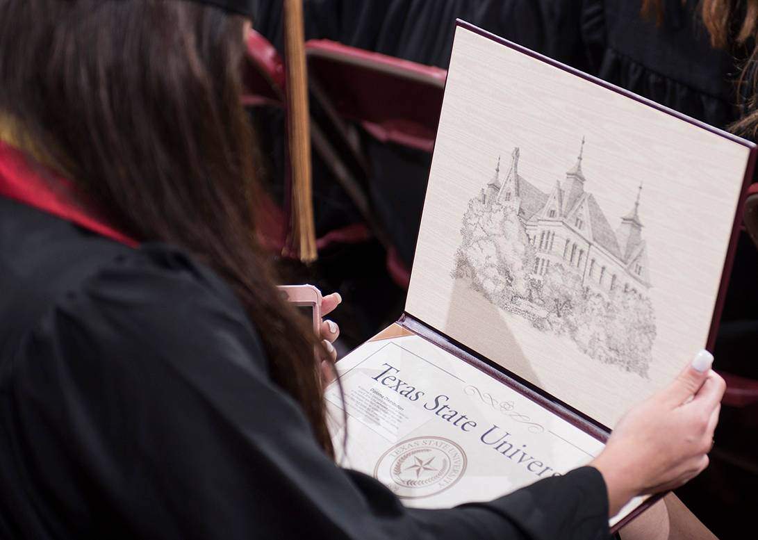 Over the shoulder of a girl opening her diploma that reads: Texas State University
