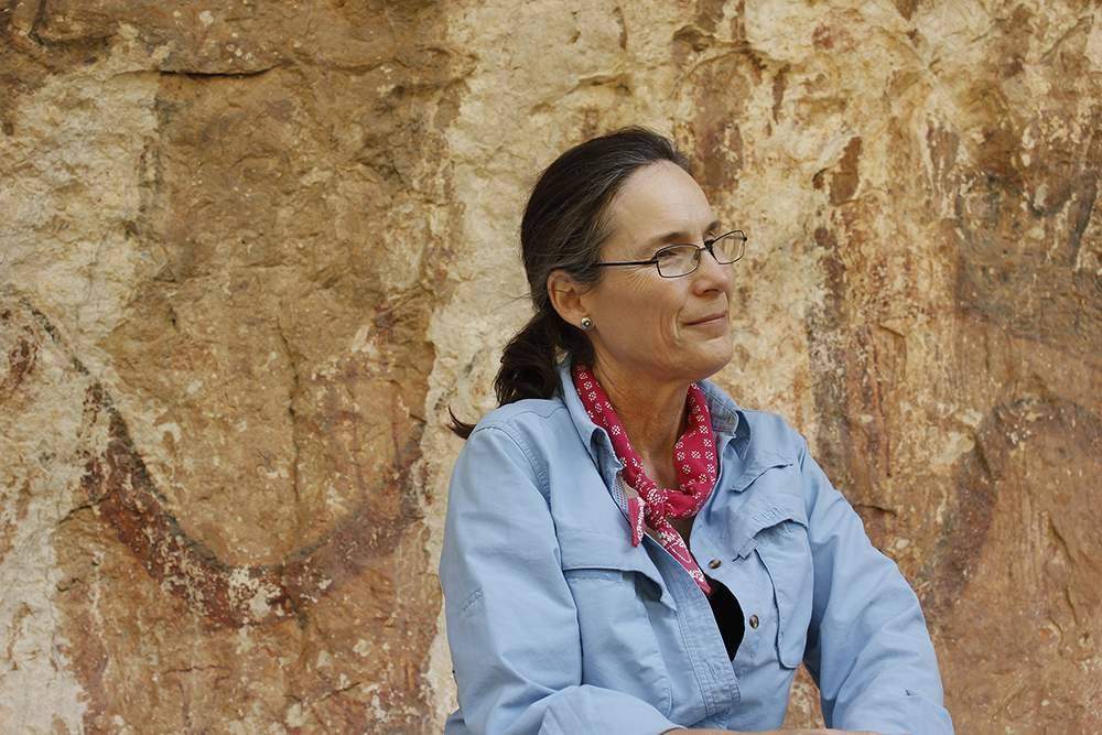 woman smiling in front of large rock formation and looking off to side