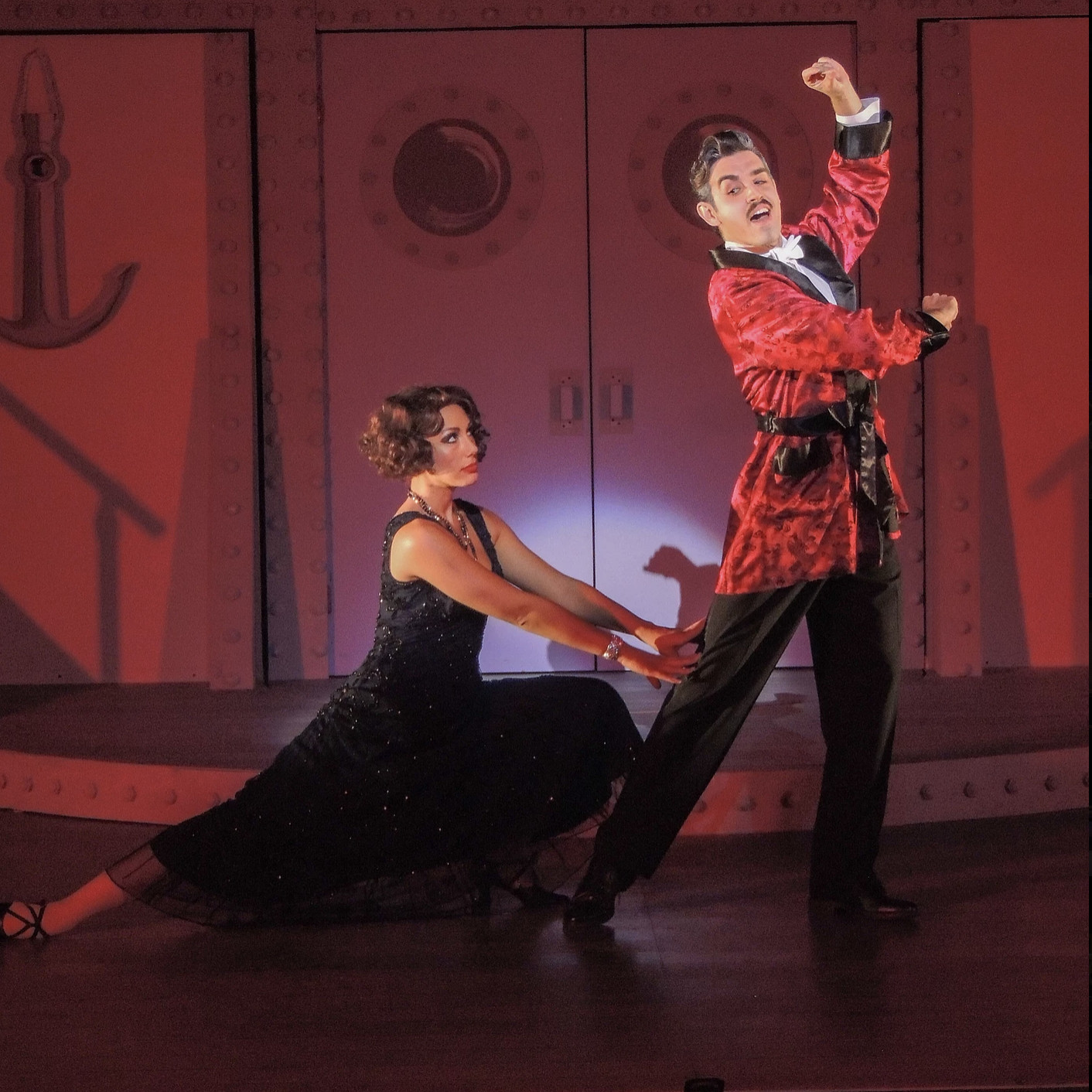 Woman in black dress dancing with suave man in red robe- they dancing tango