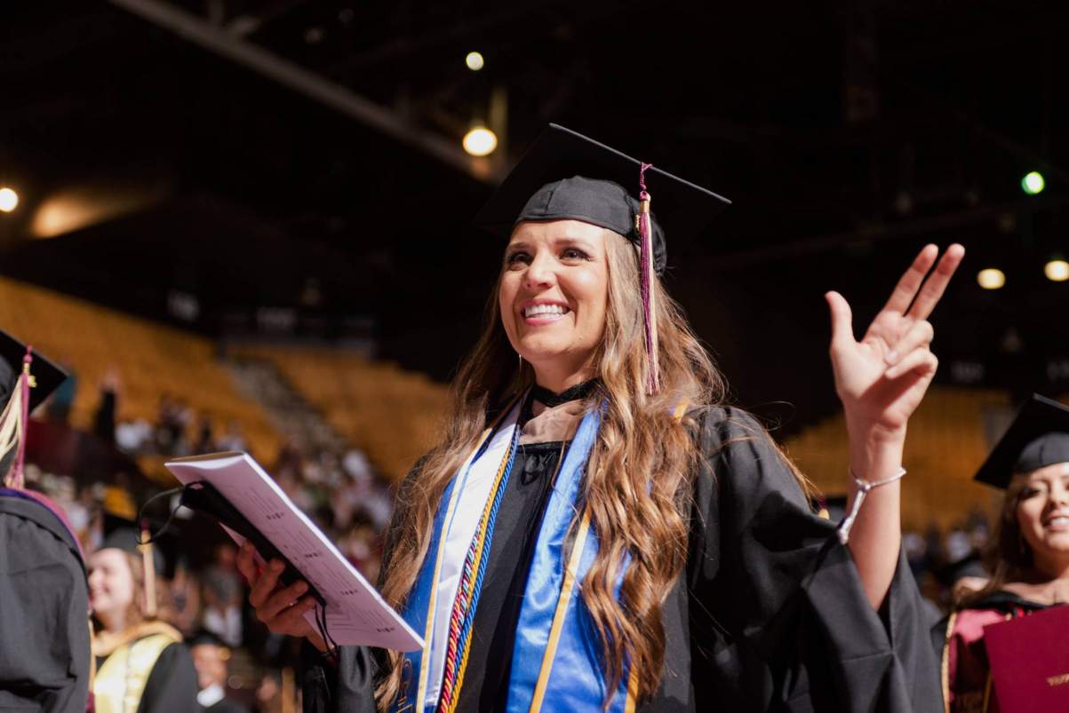 Graduate Student at commencement in robes holding up the texas state hand symbol