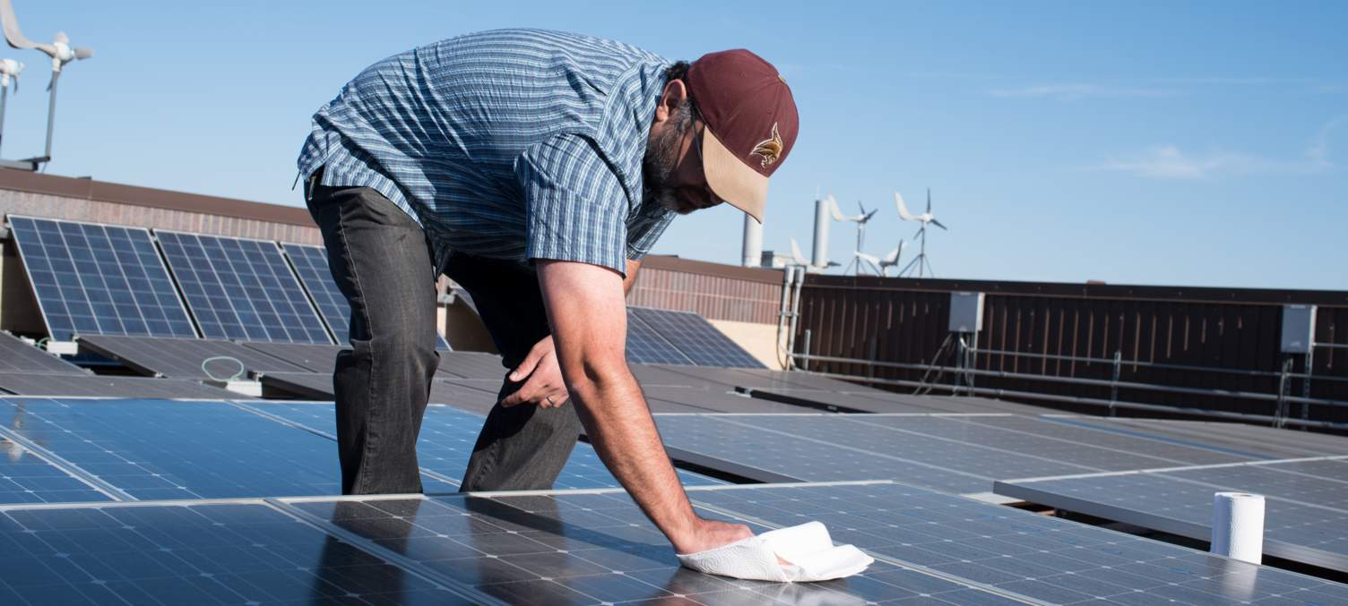 Dr. Semih Aslan cleans off a solar panel with a rag and water