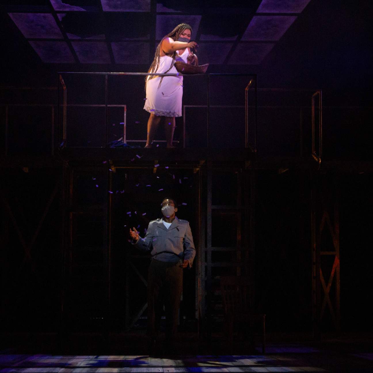 A young girl in her underclothes stands on a platform above a young man in a reformatory uniform. She holds a basket of purple petals and sings as she drops some of them on to him. He looks up at her in awe.