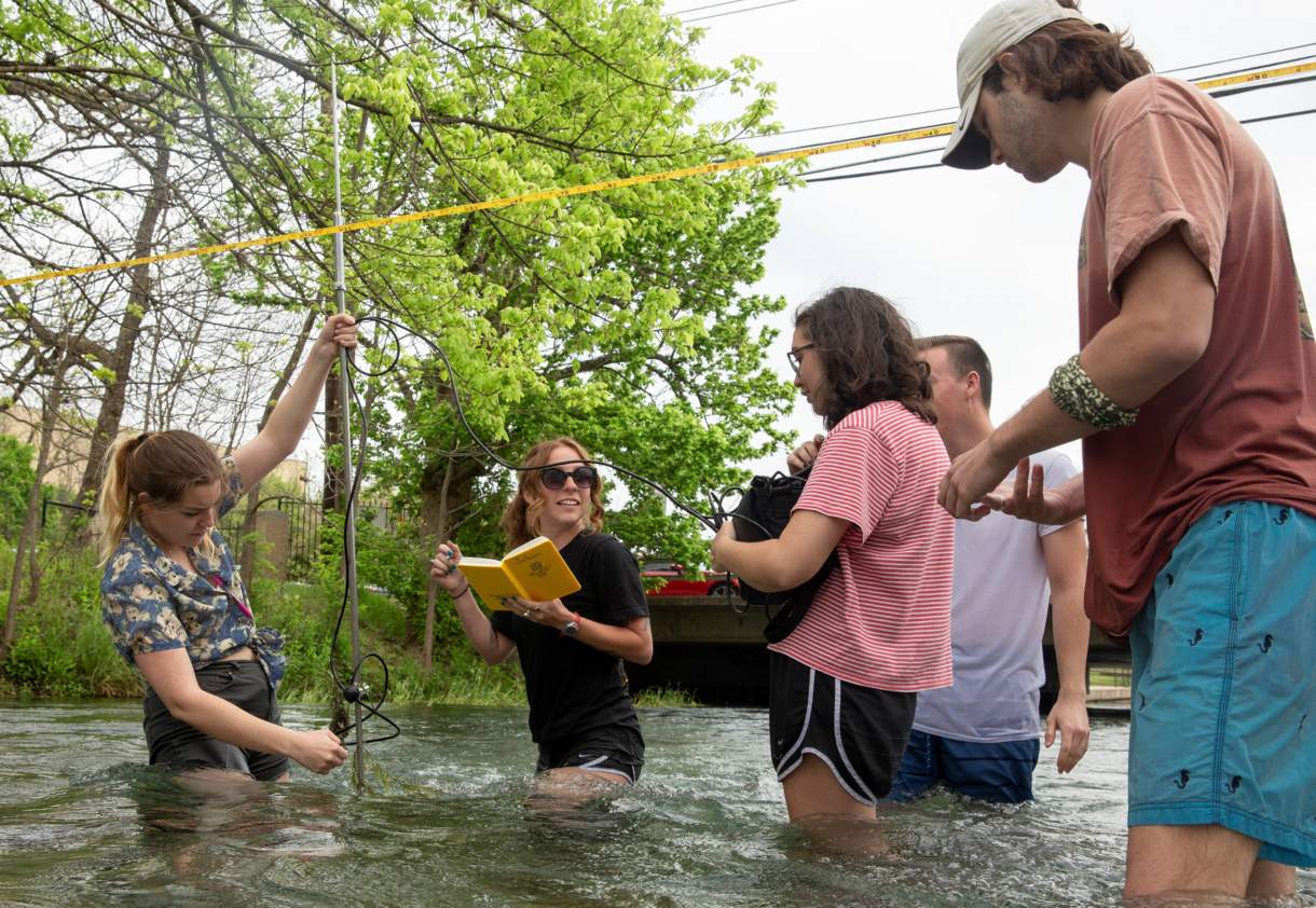 Five students conducting water quality resarch in river 