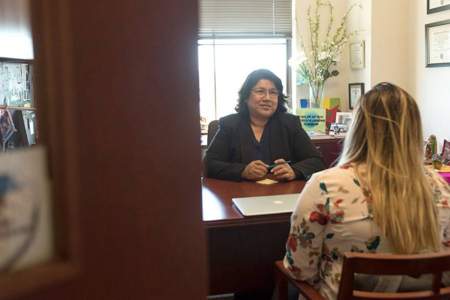 from outside the office door, we see a Latina professor meeting with a student at her desk