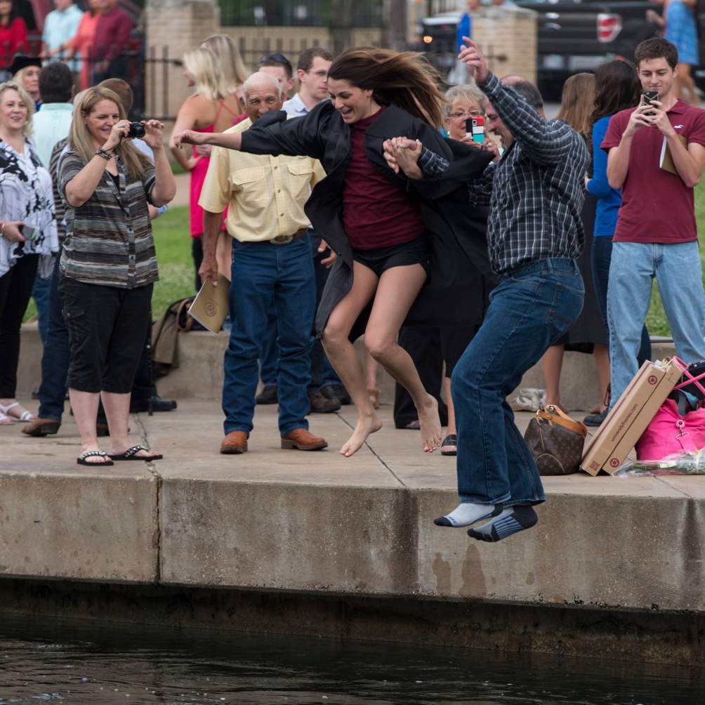 A father joins his daughter in the Texas State University tradition of jumping into the San Marcos River after a Spring 2016 commencement ceremony.