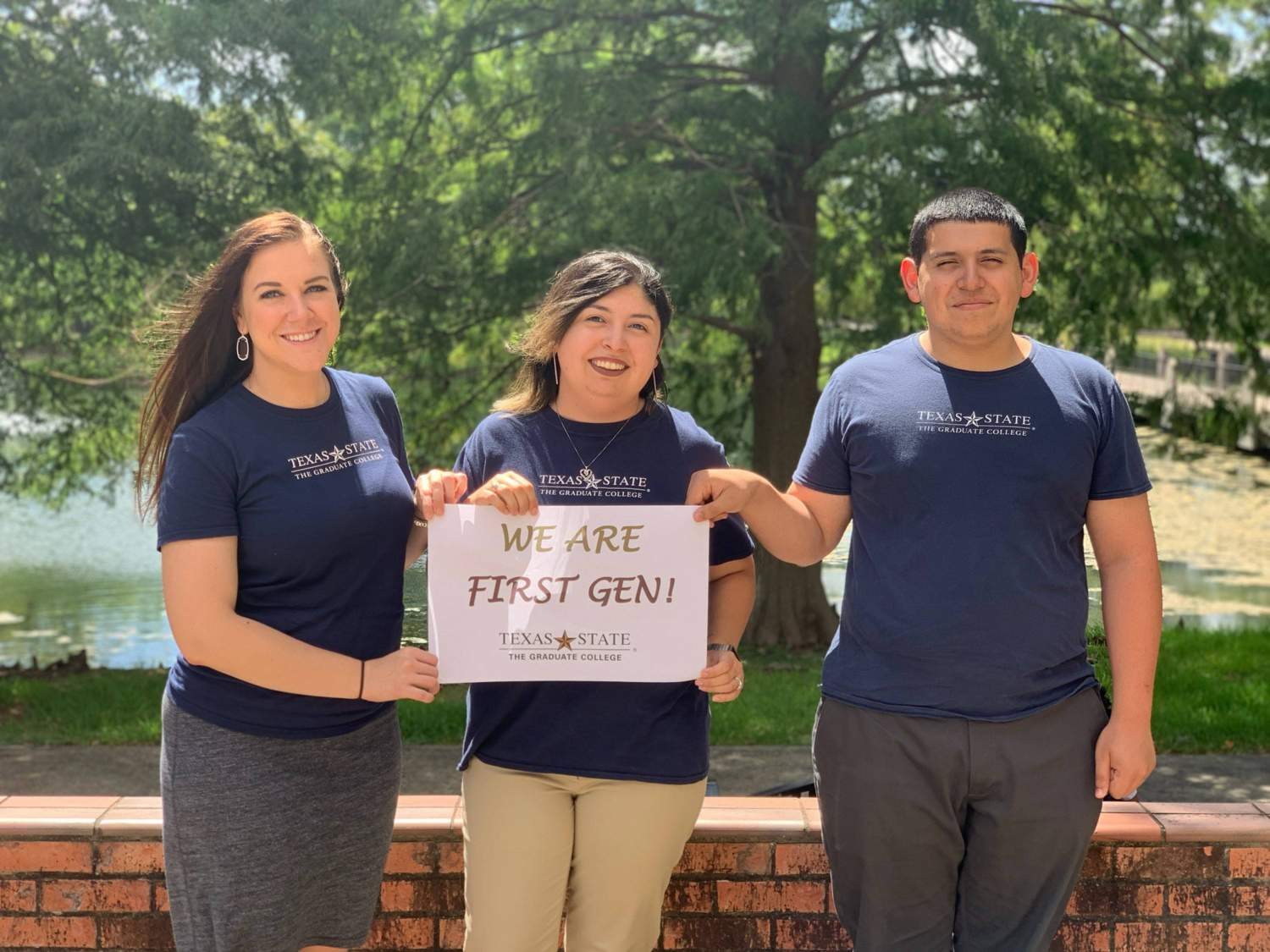 Three first-generation staff members from The Graduate College smile while holding a sign that says "We are first-gen!" 