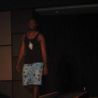 Male student/model wearing beach attire walking down the runway at the fashion show.
