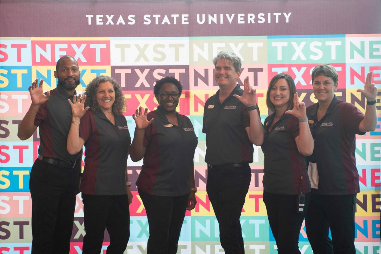 Staff in front of TXST NEXT banner