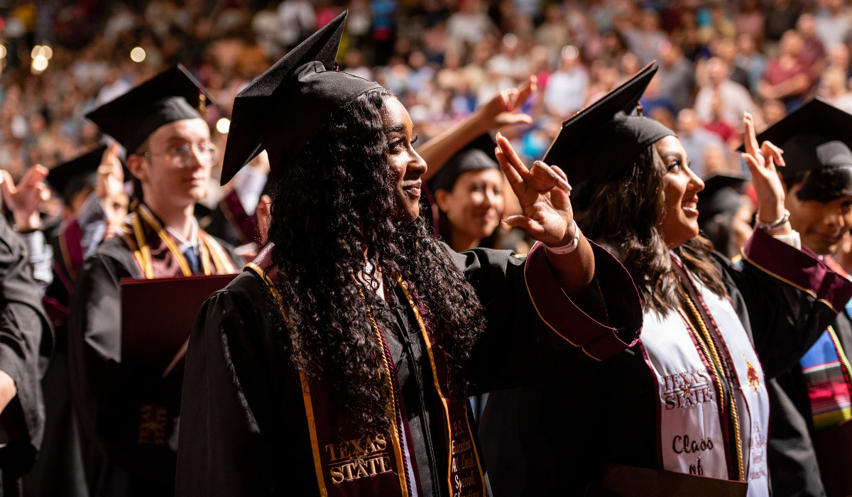 two females holding up texas hand sign at TXST commencement