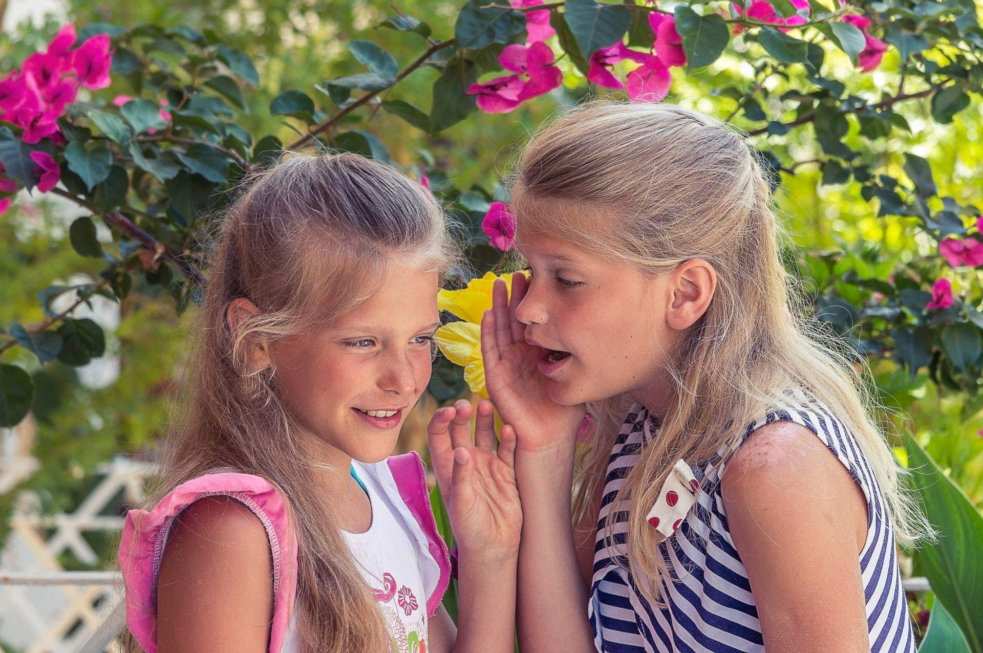 little girl whispering into another girl's ear